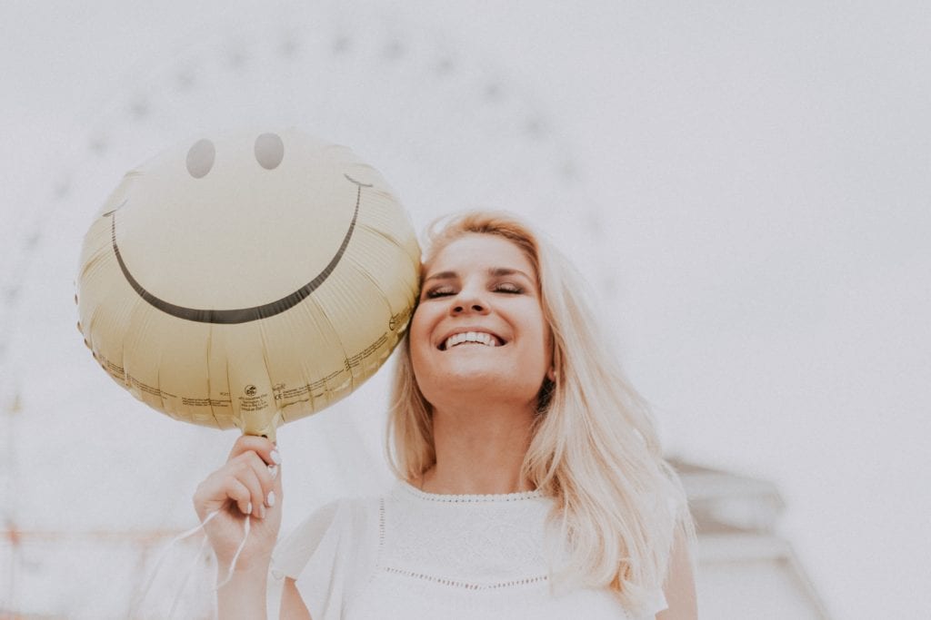 Smiling woman holding a balloon with a happy face on it.
